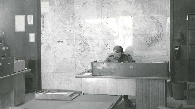 CAPT S Zagon, SPO at AUM 352, at his desk in the processing room at Nui Dat. Also shown are the main map of Phuoc Tuy Province (on which ARDF results etc., are plotted) and the direct phone to TAG G2 (INT) - Jan 1969