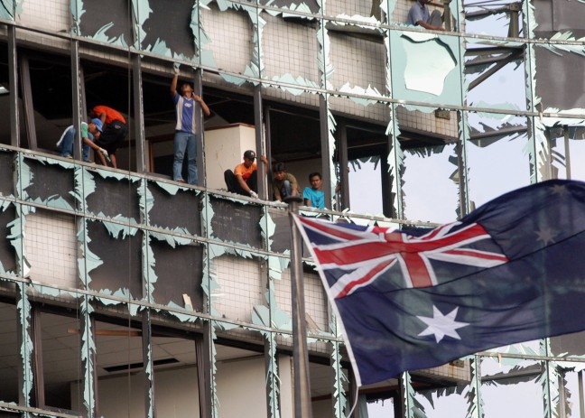 An Australian flag flying in front of the shattered windows of an office building.