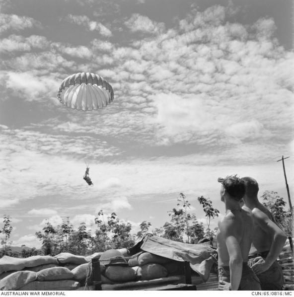 Two unidentified soldiers from 3rd Battalion, The Royal Australian Regiment (3RAR), watch as supplies float down via parachute to the landing zone (LZ) of their forward company base. As no roads link the forward bases, all supplies have to be airlifted or brought in by helicopter.