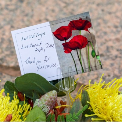 Card on floral wreath with message, ‘Lest We Forget. Lieutenant Kyle, RAN. Thank you for your service.’ 