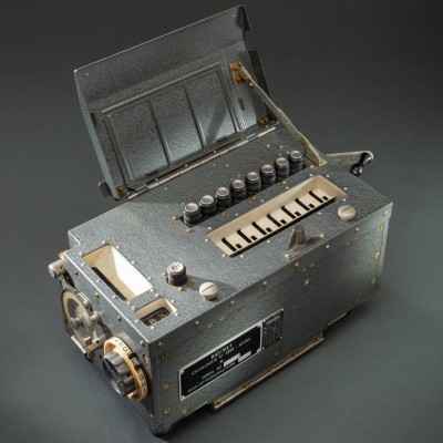 Metal encryption machine with rotors on top and a wheel with the alphabet around the edge on the side.